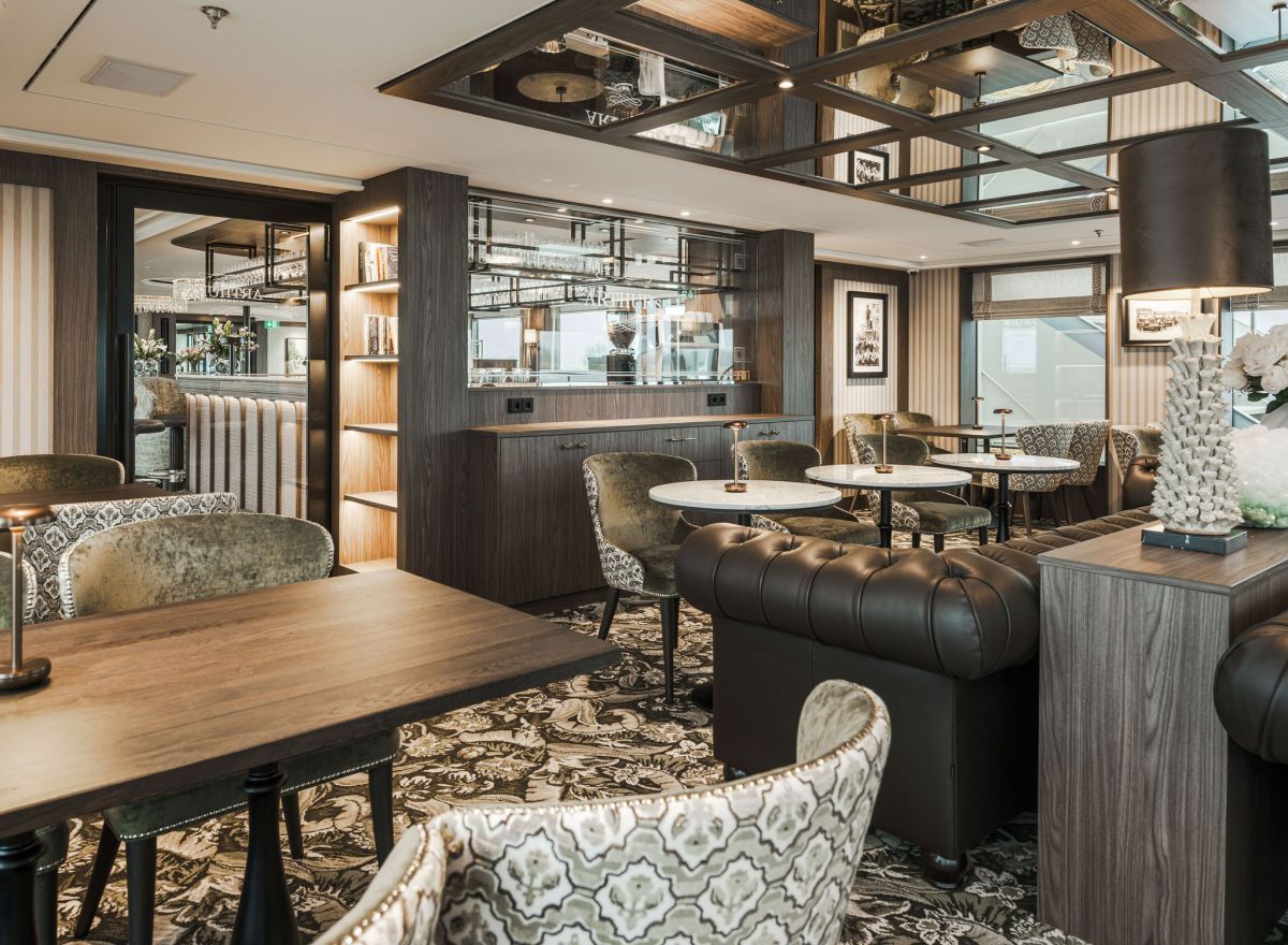 Elegant onboard restaurant with marble tables, patterned chairs, blue accents, and panoramic windows overlooking the river.