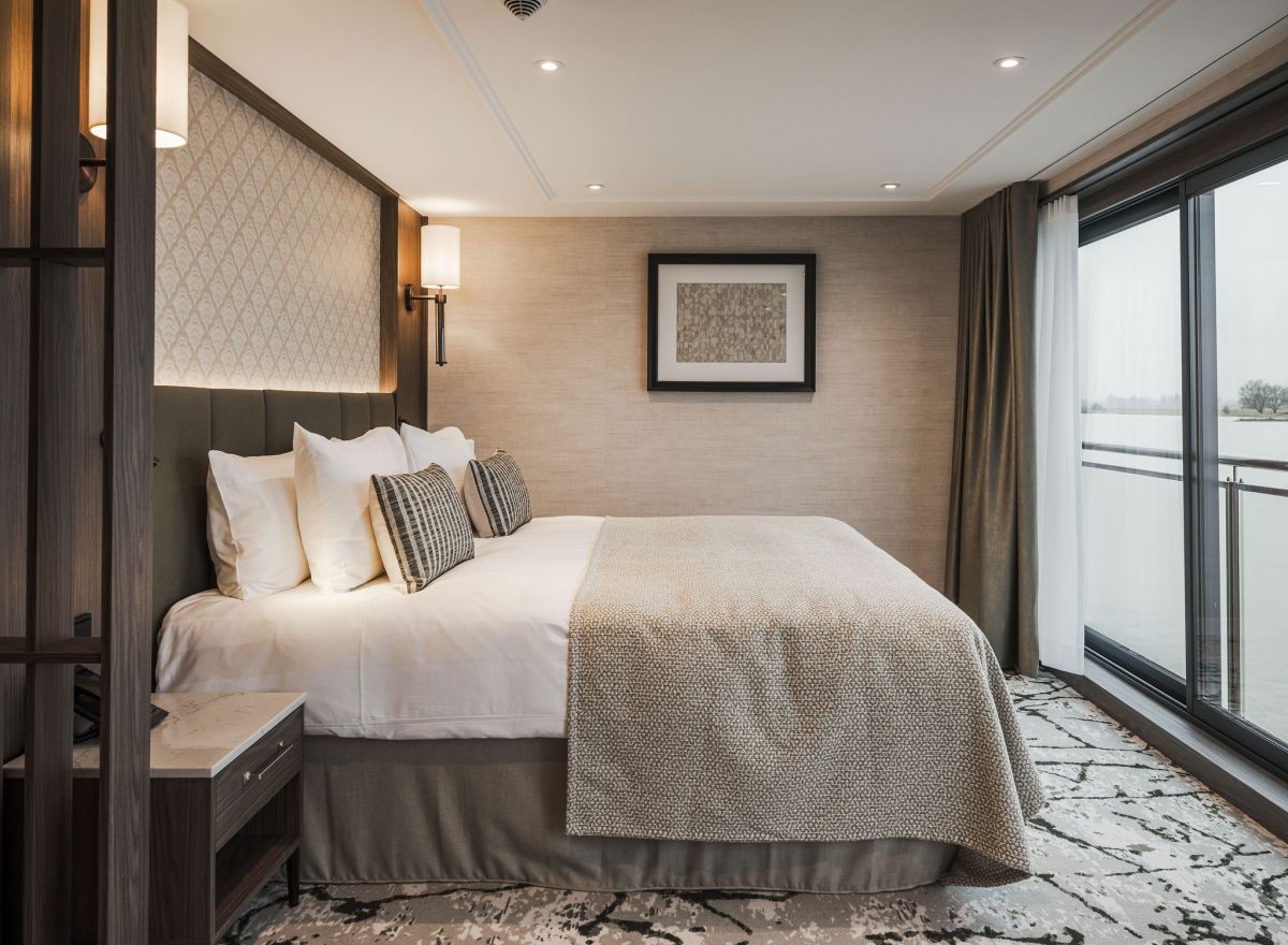 Luxurious river cruise cabin with a large double bed, elegant wall lamps, textured beige walls, and modern décor.